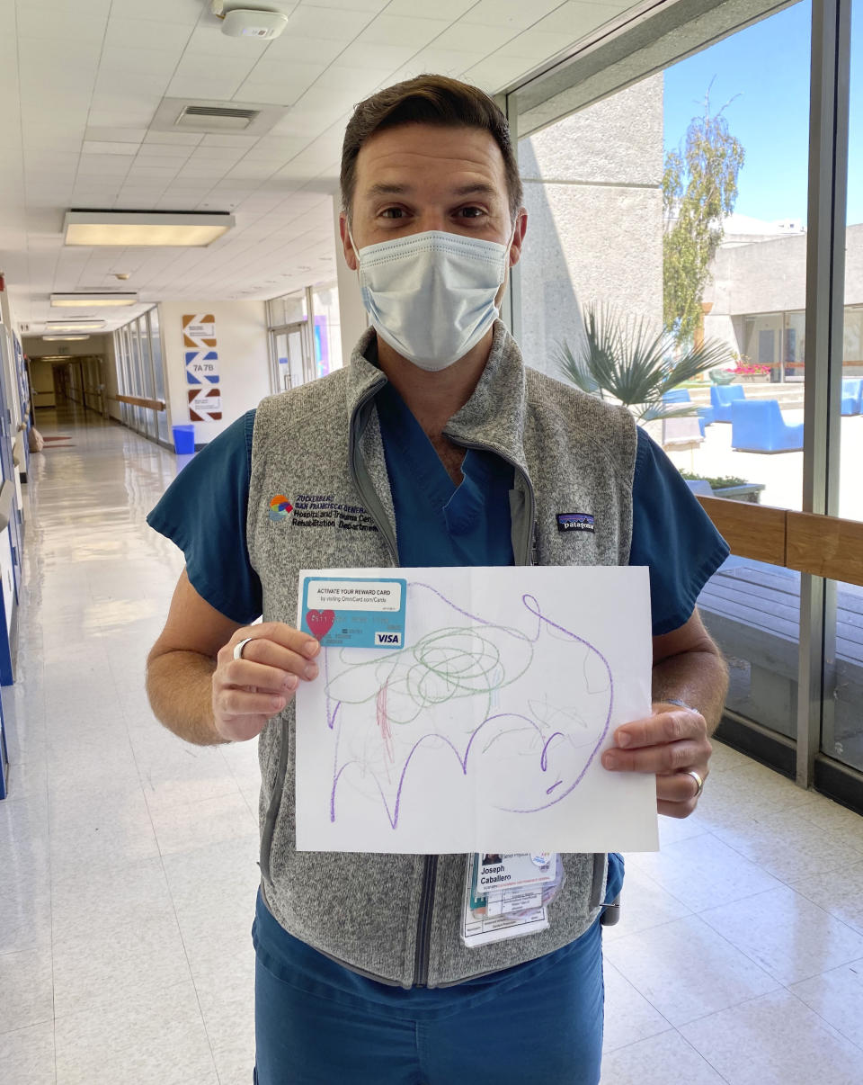 In this Aug. 3, 2020, handout photo provided by Nykole Baltazar, health care worker Joe Caballero holds a handwritten thank-you card while working at Zuckerberg San Francisco General Hospital and Trauma Center in San Francisco. Siblings Mantej Singh Lamba, 17, and Prabhleen Singh Lamba, 15, started the Cards 4 Covid Heroes initiative in May and have since delivered more than 250 cards to hospitals in California and Arizona. (Nykole Baltazar via AP)