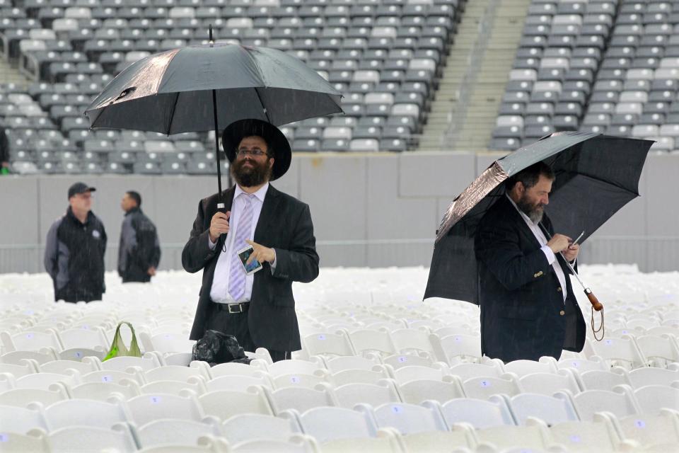 Men stand in the rain at MetLife stadium in East Rutherford, N.J, Wednesday, Aug. 1, 2012, as they wait for the start of the celebration Siyum HaShas. The Siyum HaShas, marks the completion of the Daf Yomi, or daily reading and study of one page of the 2,711 page book. The cycle takes about 7½ years to finish.This is the 12th put on my Agudath Israel of America, an Orthodox Jewish organization based in New York. Organizers say this year's will be, by far, the largest one yet. More than 90,000 tickets have been sold, and faithful will gather at about 100 locations worldwide to watch the celebration. (AP Photo/Mel Evans)