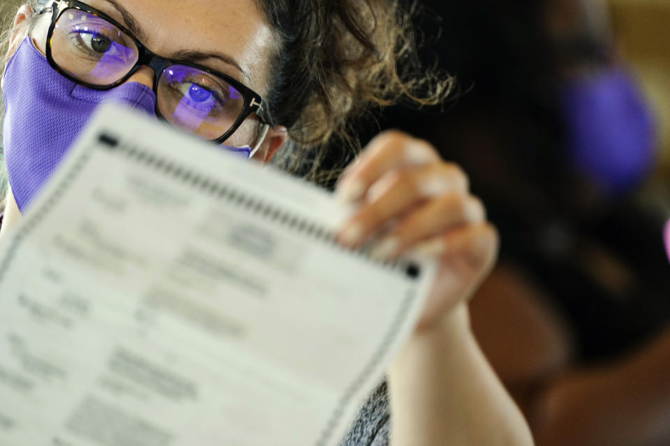 An election worker wearing a face mask examines ballots