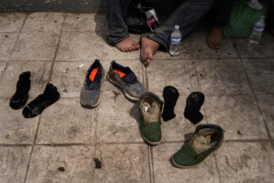 Two men from Honduras dry out their shoes after being returned from the U.S. to Mexico, Thursday, May 13, 2021, in Reynosa, Mexico. The Biden administration has agreed to let up to about 250 people a day in the United States at border crossings with Mexico to seek refuge, part of negotiations to settle a lawsuit over pandemic-related powers that deny migrants a right to apply for asylum, an attorney said Monday. (AP Photo/Gregory Bull)