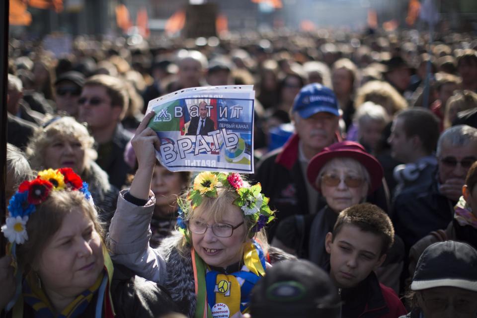 A woman, wearing a traditional Ukrainian wreath of flowers on her head, holds up a sign with President Vladimir Putin’s picture and the words: “Stop lying!” during a rally against pro-Putin media in Moscow, Russia, Sunday, April 13, 2014. More than 10,000 people have turned out in Moscow for an anti-Kremlin rally to denounce Russian state television’s news coverage, particularly of the crisis in neighboring Ukraine. (AP Photo/Alexander Zemlianichenko)