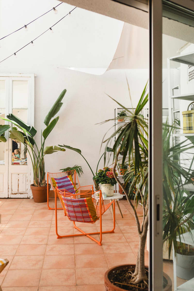 White outdoor area with lots of plants, small table with orange chairs