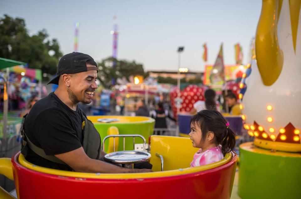 Anthony Candelaria, de North Highlands, y su hija  Annalise Candelaria, de 2 años, montan en las tazas de té en la Feria del Condado de Sacramento en Cal Expo en 2023.