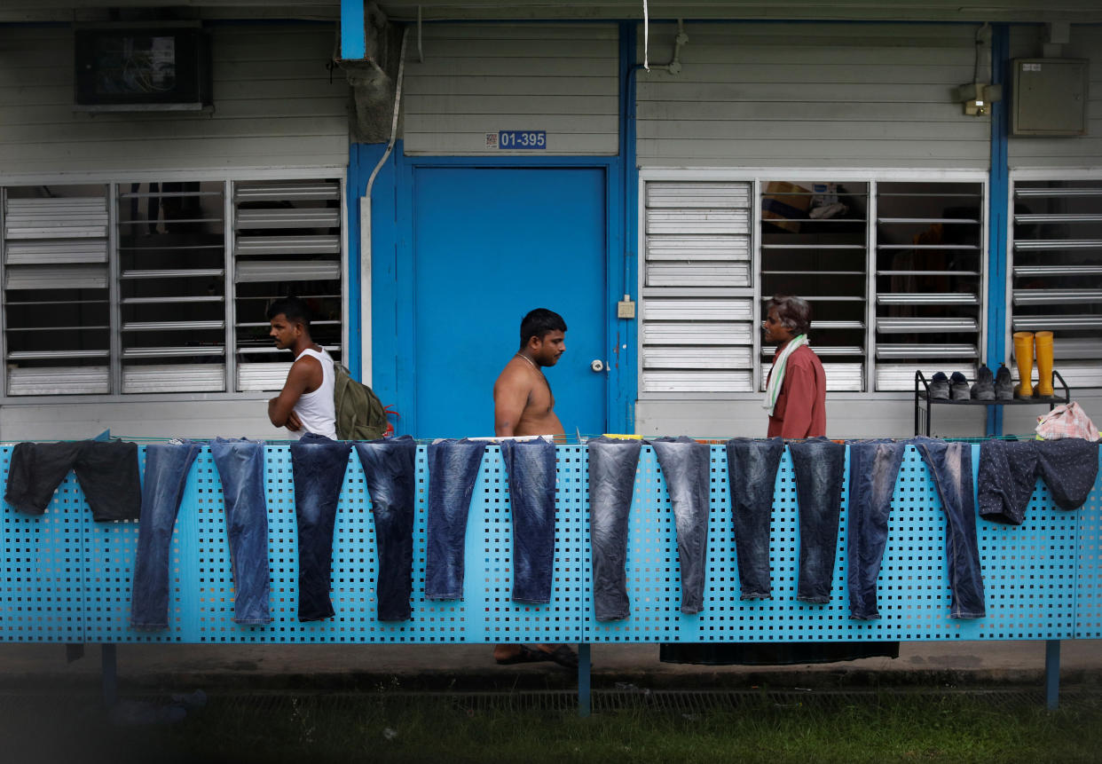 Workers pass a row of pairs of jeans hung to dry at S11 Dormitory @ Punggol, which was gazetted to be an isolation facility, on 6 April, 2020. (PHOTO: Reuters)