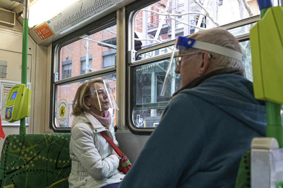 Two commuters wearing face shields are seen as they travel by tram during lockdown in Melbourne, Australia, Wednesday, Aug. 5, 2020. Victoria state, Australia's coronavirus hot spot, announced on Monday that businesses will be closed and scaled down in a bid to curb the spread of the virus. (AP Photo/Asanka Brendon Ratnayake)