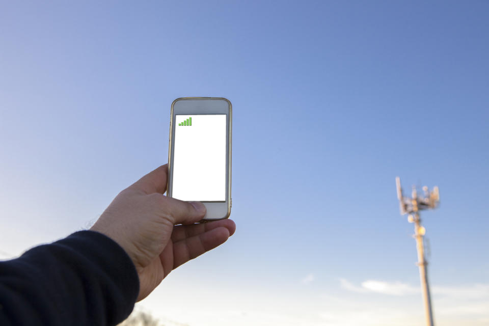 A man holds a smartphone up next to a cellular tower.