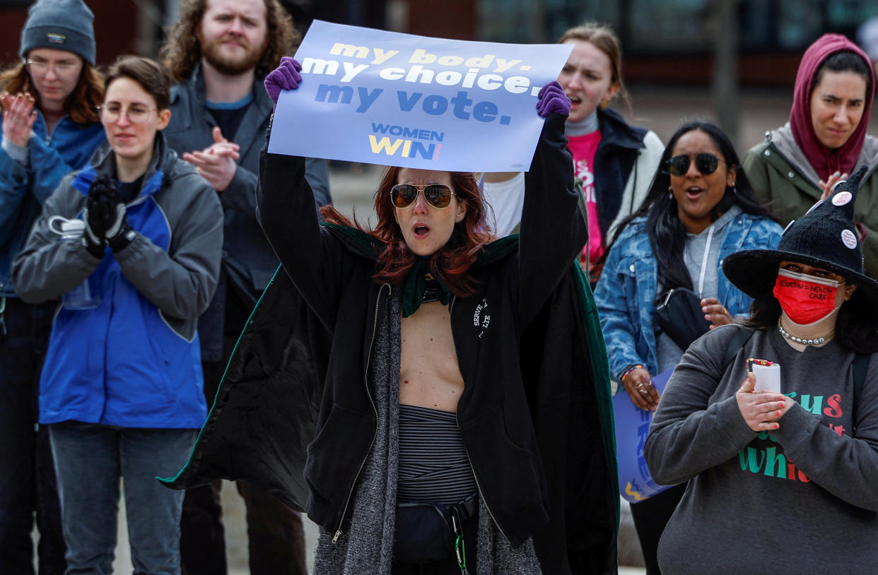 A half a dozen protesters stand around one person holding a sign that reads: My body, my choice, my vote. Women win.