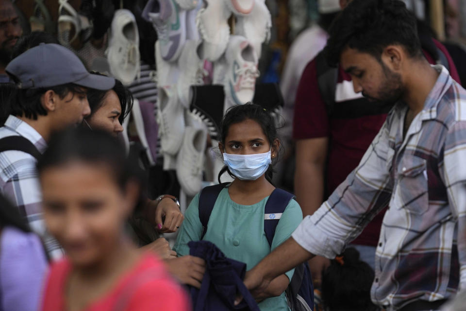 People walk past a girl wearing a face mask in a shopping district of Mumbai, India, Thursday, Dec. 22, 2022. India has begun randomly testing international passengers arriving at its airports for COVID-19, the country’s health minister said Thursday, citing an increase in cases in neighboring China and also asked the public to wear masks and maintain social distancing. (AP Photo/Rafiq Maqbool)