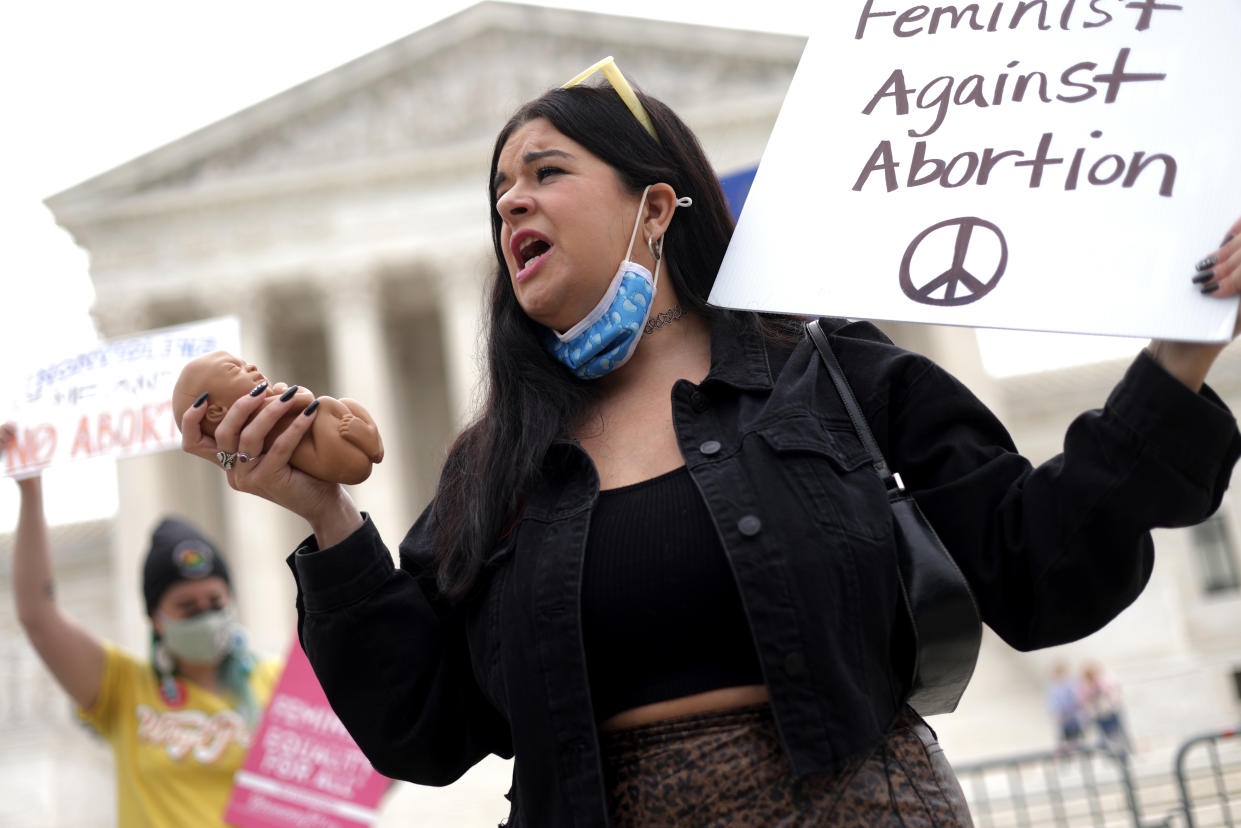 A demonstrator holds a sign reading: Feminist Against Abortion with a peace sign.