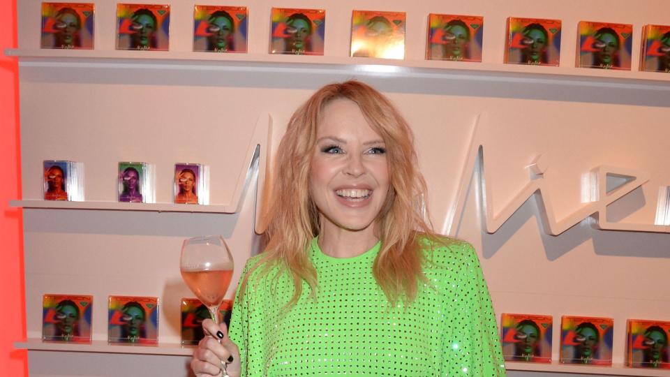 Kylie Minogue in sparkly green dress holding wine glass 