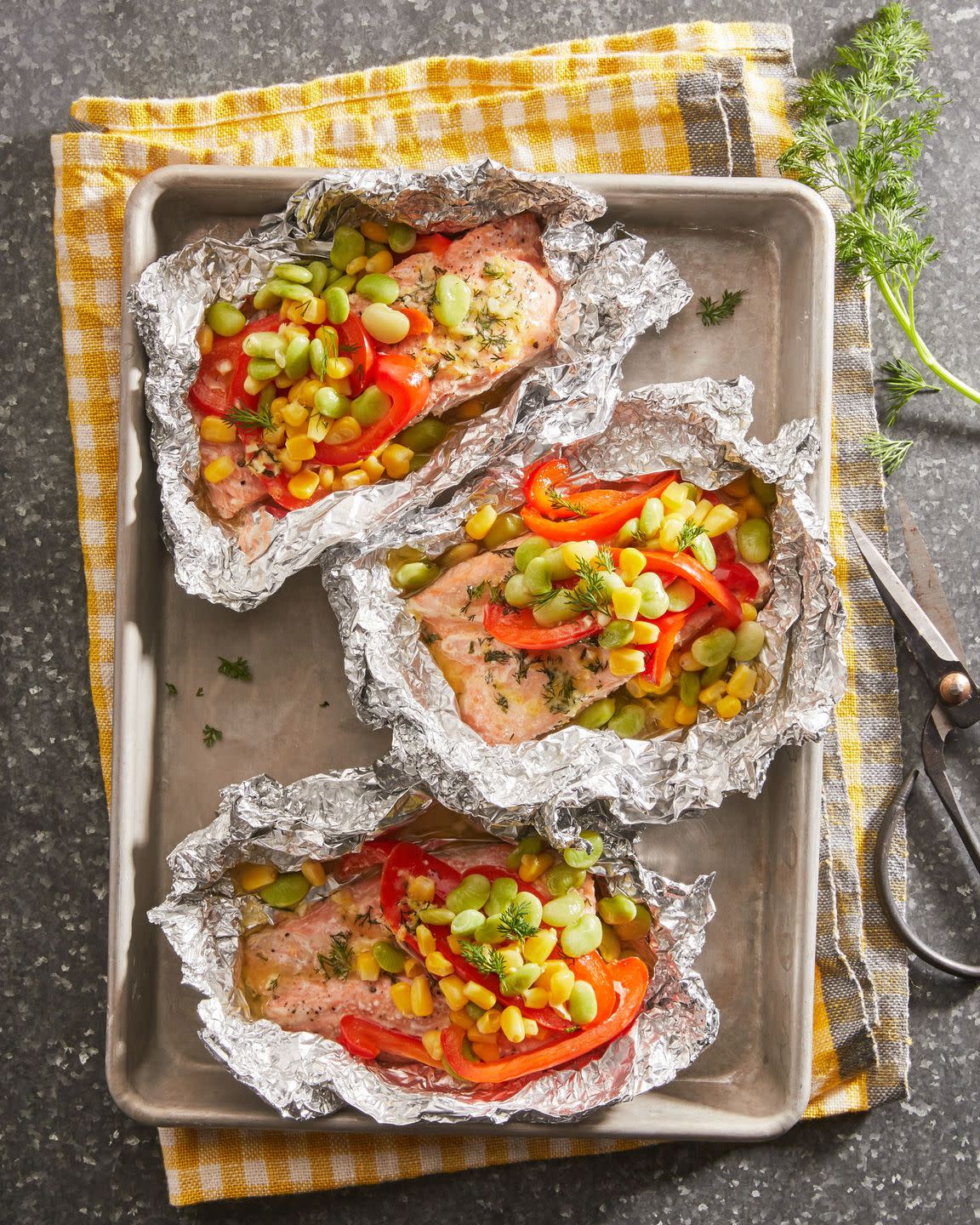 salmon in foil with vegetables on a sheet tray