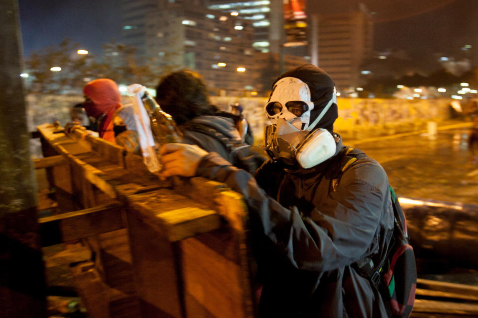 A protester wearing a painter's mask helps build a barricade against the advance of a police water cannon in the Altamira neighborhood of Caracas, Venezuela, Wednesday, Feb. 19, 2014. The opposition is protesting the Tuesday detention of thier leader Leopoldo Lopez, as well as rampant crime, shortages of consumer goods and an inflation rate of more than 50 percent. (AP Photo/Alejandro Cegarra)