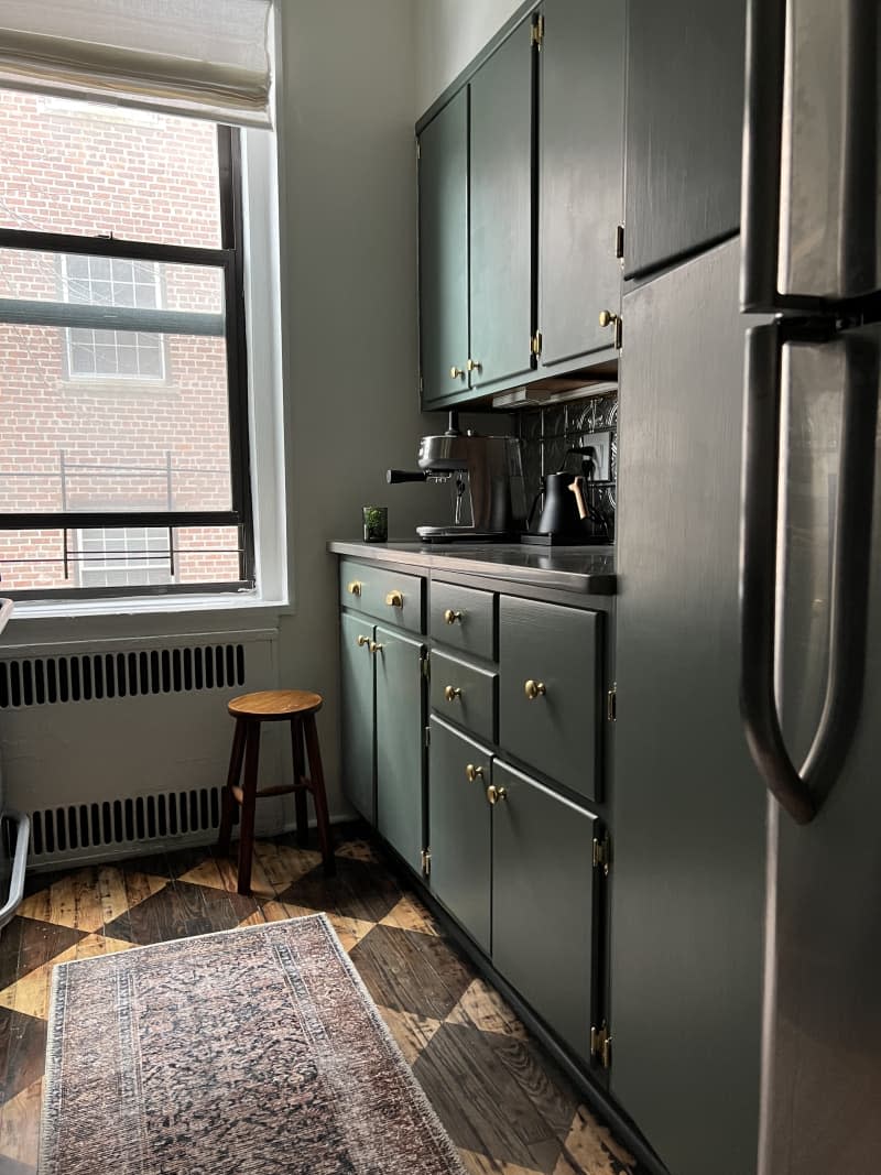 Dark green painted kitchen cabinets with gold knobs.