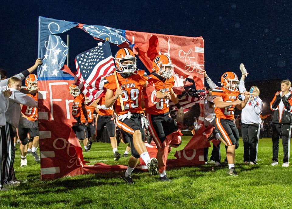 Kye Aken, 29, Kyle Jones, 84, and Jacob Ross, 23, lead the Byron Tigers onto the field before their game against Dixon on Friday, Oct. 13, 2023, in Byron.