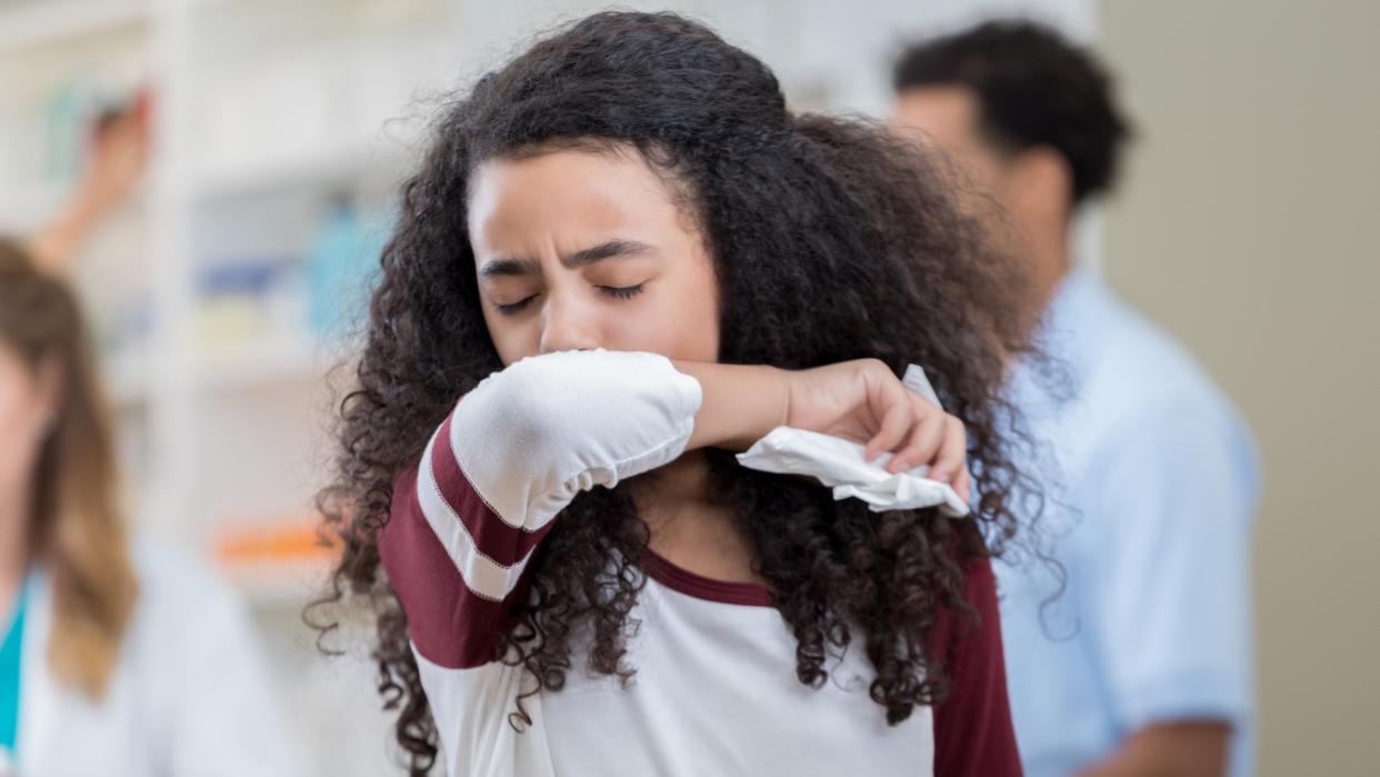  Young person of color preteen girl sneezes into her arm in pharmacy. 