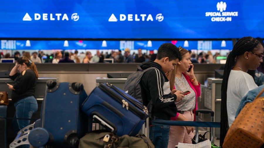 People line up with bags with a Delta check in banner visible in the background