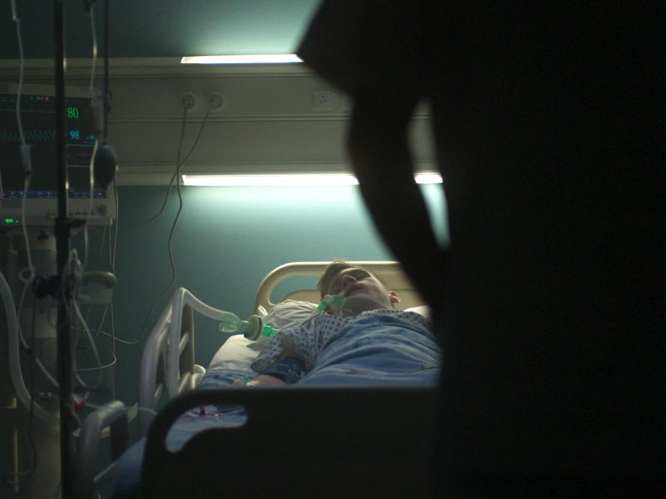 An ominous silhouette of a nurse looking at a patient on a ventilator