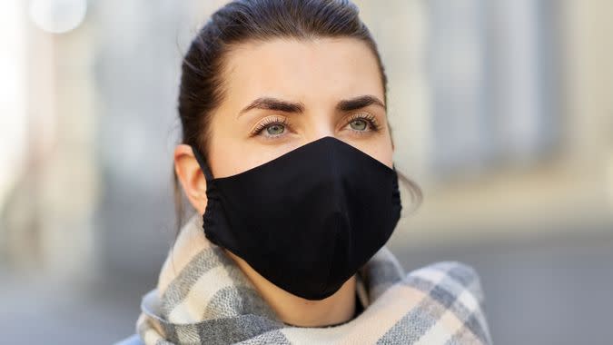 health, safety and pandemic concept - young woman wearing black face protective reusable barrier mask outdoors