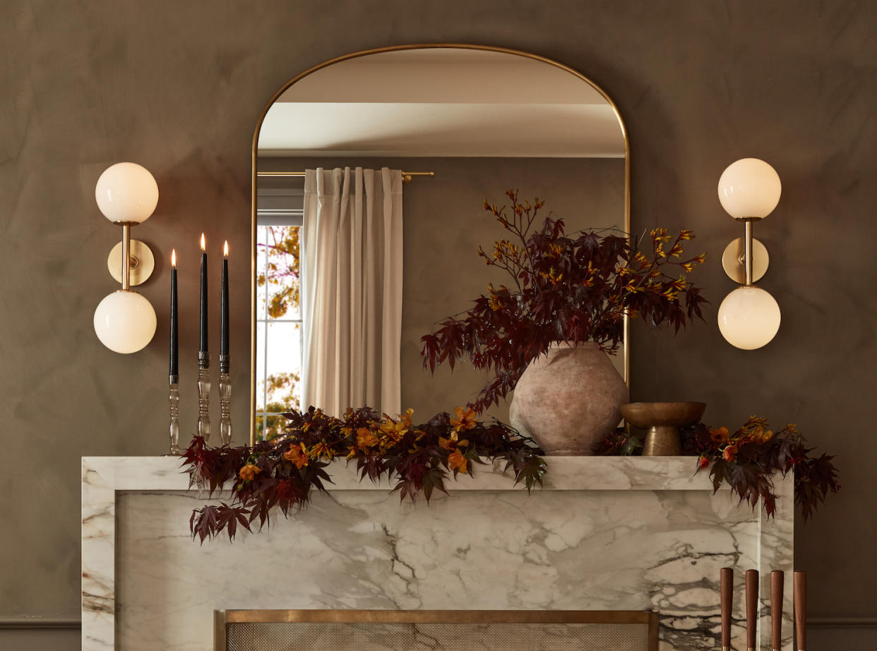  A marble fireplace decorated with a mirror, dried flowers and two wall lights. 