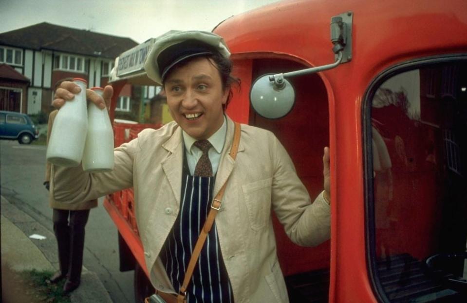 Man in vintage delivery outfit with milk bottles by a red van