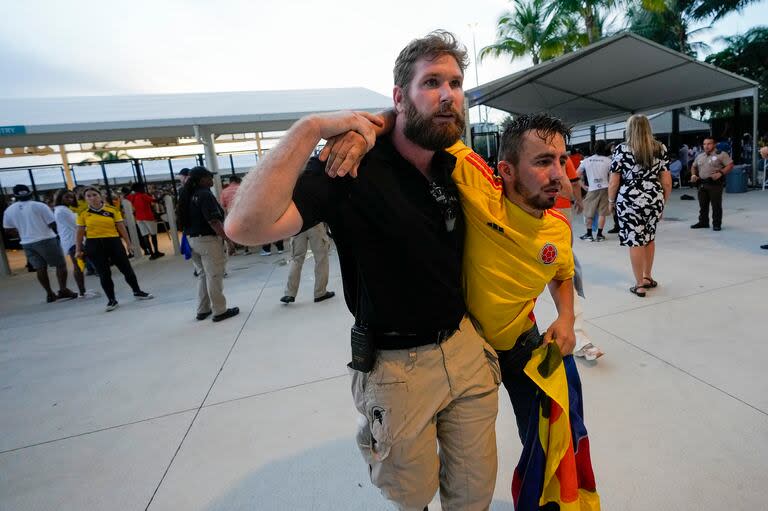 Un agente de seguridad ayuda a un hincha colombiano que esperaba entrar al estadio antes de la final de la Copa América