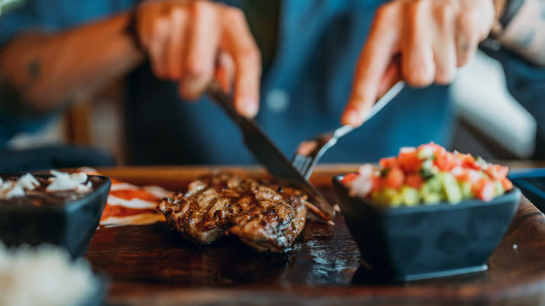 person cutting steak with sides