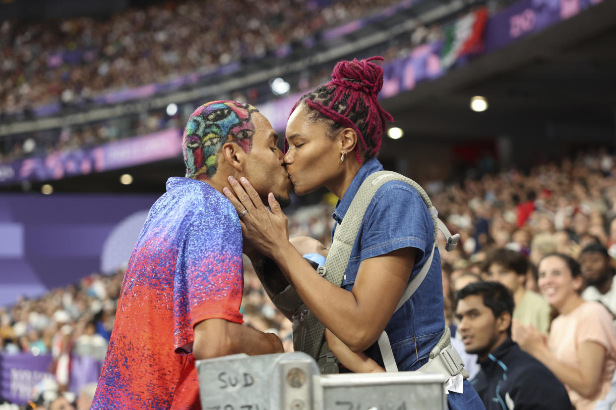 Roderick Townsend of the United States kisses his wife Tynita Townsend, with their son Rodney Townsend, between Rodrick's jumps in the T47 Men's High Jump at the 2024 Paralympics, Sunday, Sept. 1, 2024 in Paris, France. (AP Photo/Caleb Craig)