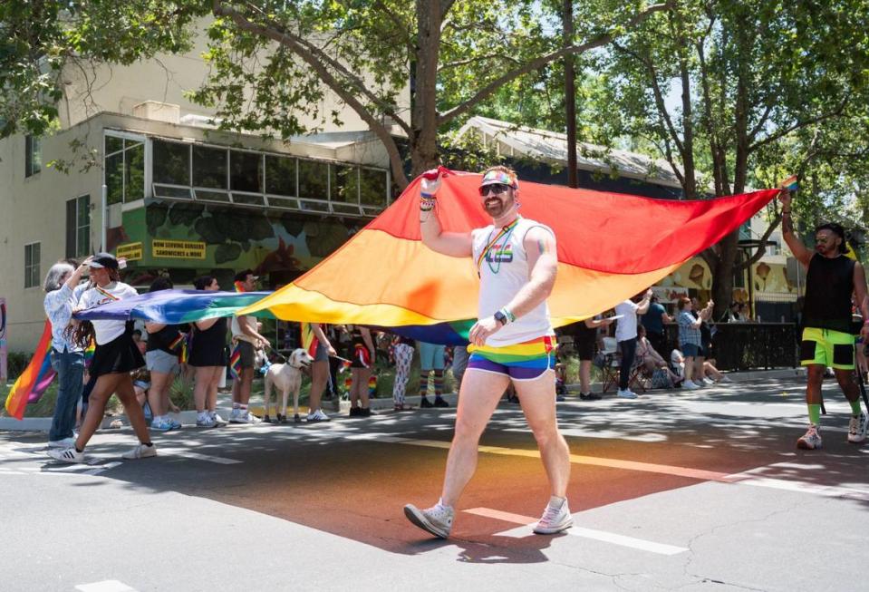 Un grupo de participantes en el desfile del domingo portan una bandera de arco iris a lo largo de Q Street, en el centro de Sacramento, con motivo de la Marcha del Orgullo que se celebra anualmente . Algunos participantes repartieron preservativos y otros, calcomanías u otros artículos con los colores del arco iris.