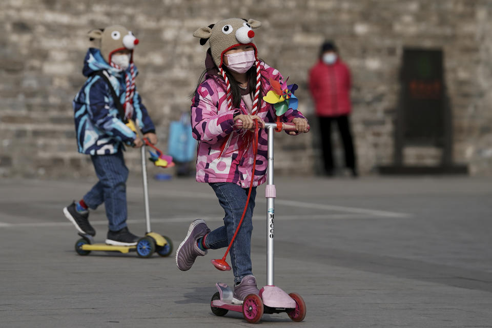 Children wearing a protective gear to help curb the spread of the coronavirus play with their scooter in Beijing, Wednesday, Jan. 27, 2021. China has given more than 22 million COVID vaccine shots to date as it carries out a drive ahead of next month's Lunar New Year holiday, health authorities said Wednesday. (AP Photo/Andy Wong)