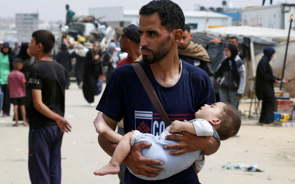 A man carries a child, as Palestinians travel on foot along with their belongings as they flee Rafah