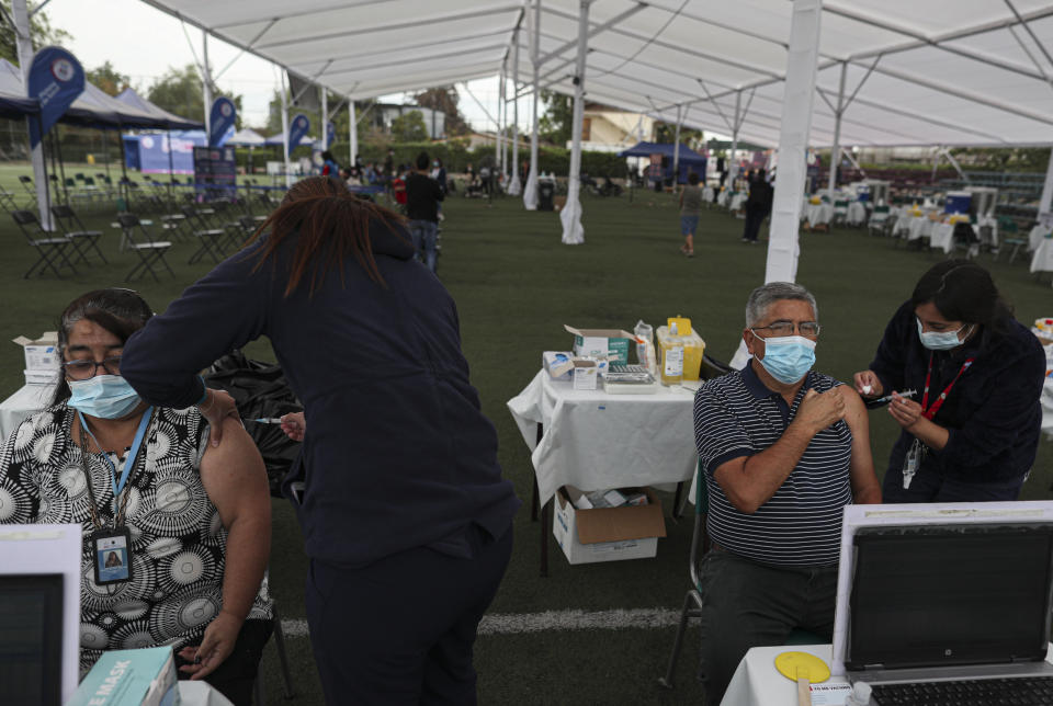 Healthcare workers inject people with the Sinovac COVID-19 vaccine at La Pintana Sports Complex turned into a makeshift vaccination site, in Santiago, Chile, Thursday, March 11, 2021, on the one-year anniversary that the World Health Organization declared the coronavirus a pandemic. (AP Photo/Esteban Felix)