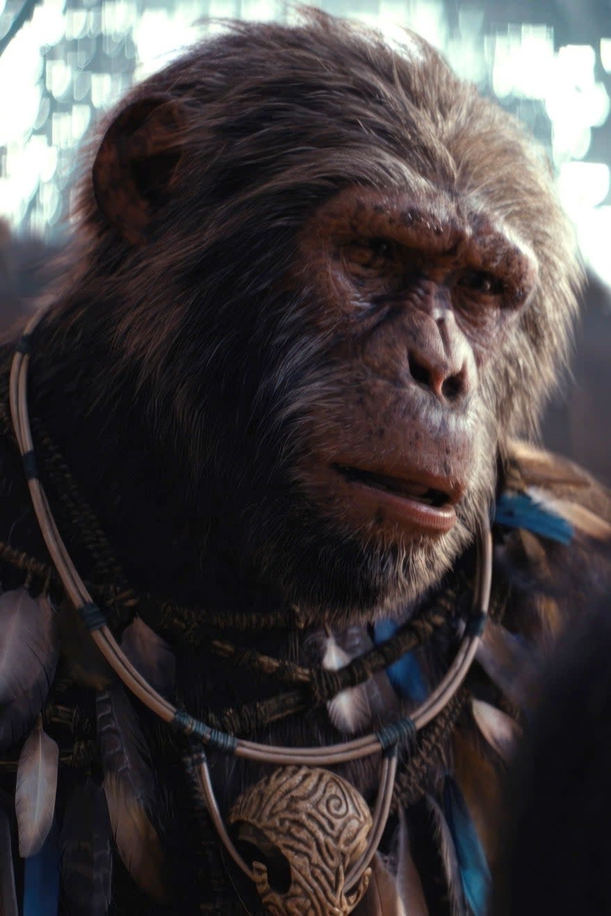 Koro wearing white-and-blue feathers and a necklace while speaking to Noa in Kingdom of the Planet of the Apes