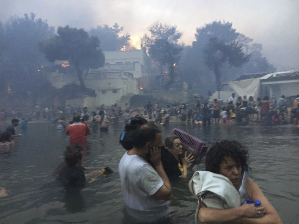 In this Monday, July 23, 2018 image from video provided by Elia Kallia, people escaping wildfires wade into the waters of the "Silver Coast" beach in Mati, Greece. Dozens were either killed by flames or drowned as they tried to flee the fire into the nearby sea, waiting for hours in the water for rescue from local fishermen and other boat owners. (Elia Kallia via AP)