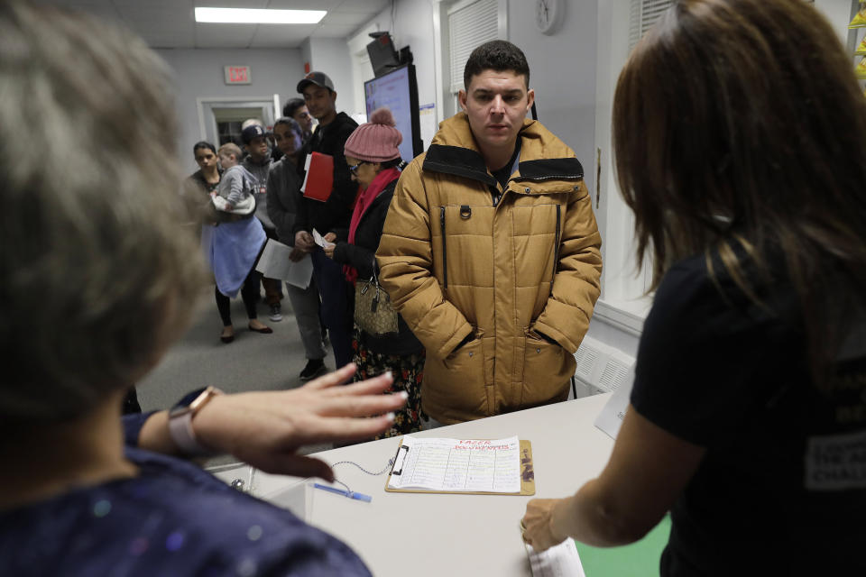 In this Wednesday, Dec. 4, 2019 photo Helison Alvarenga, of Brazil, center, speaks with volunteers Marcia Previatti, front left, and Arlene Vilela, front right, at the New England Community Center, in Stoughton, Mass. Alvarenga, a 26-year-old from the Brazilian state of Minas Gerais, arrived in Massachusetts about four months ago after crossing the Mexican border at Juarez with his 24-year-old wife, Amanda, and 6-year-old son, David. The family were at the community center Dec. 4, to apply for new Brazilian passports, which Alvarenga says were seized by border officials. (AP Photo/Steven Senne)