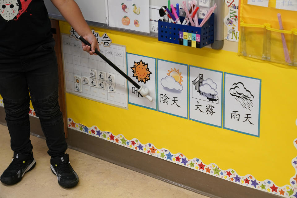 In Suzy Tom's first grade class a student points at pictures and characters on a wall at the Alice Fong Yu school in San Francisco, Tuesday, Aug. 30, 2022. The school is the nation's first Chinese immersion public school and provides Cantonese instruction from kindergarten until the 8th grade. While Cantonese may be on a downward trajectory, it's not dying. Online campaigns, independent Chinese schools and Cantonese communities in and outside of Chinatowns are working to ensure future generations can carry it forward. (AP Photo/Eric Risberg)