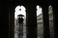 A couple shelter against the rain with an umbrella as they walk in St. Mark's Square during a rainy day in Venice, Sunday, March 1, 2020. (AP Photo/Francisco Seco)