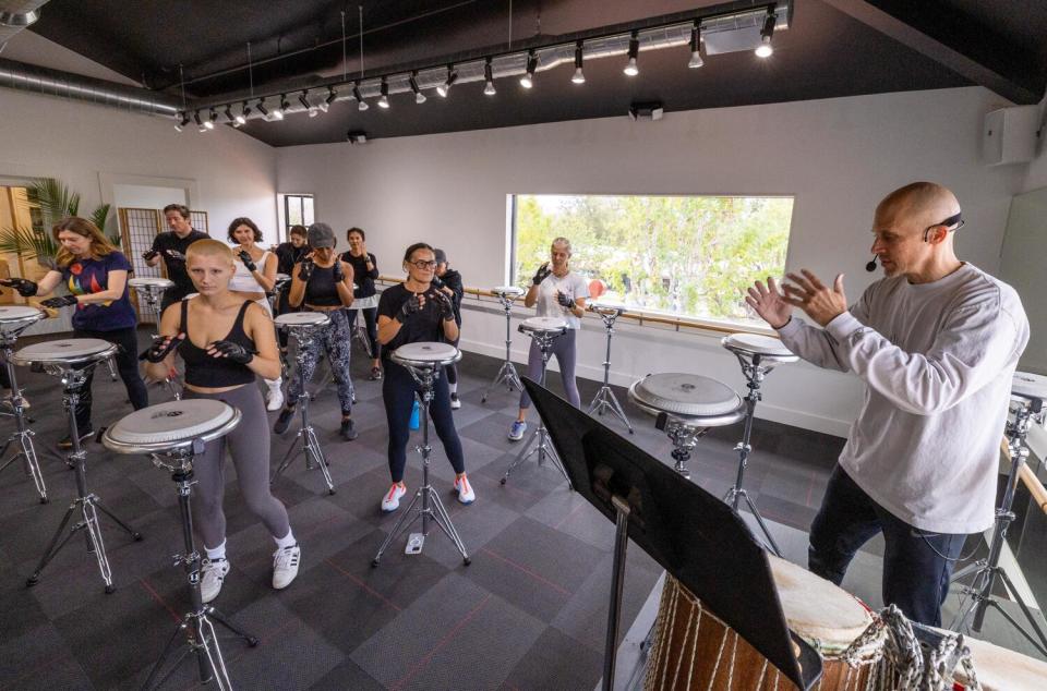 People gather around conga drums on thin pedestals in a light-filled room, ready to bounce to the next move.