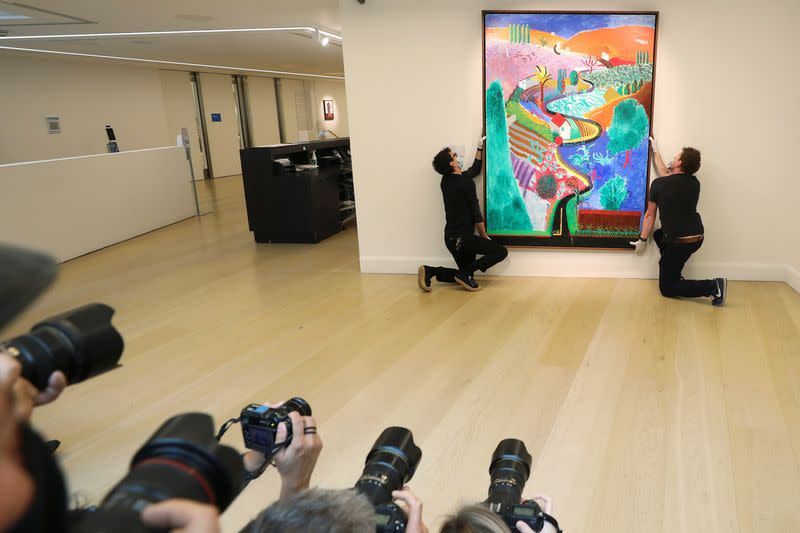 Members of the media photograph employees adjusting a painting by David Hockney entitled 'Nichols Canyon' which has an estimated value of $35 million at Phillips auction house in London