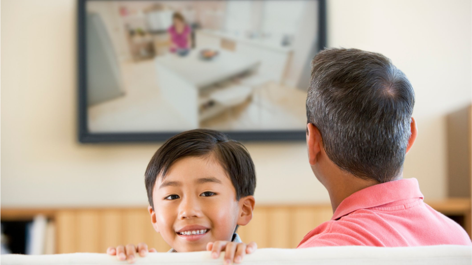 Kid looks at the camera while his father watches the screen