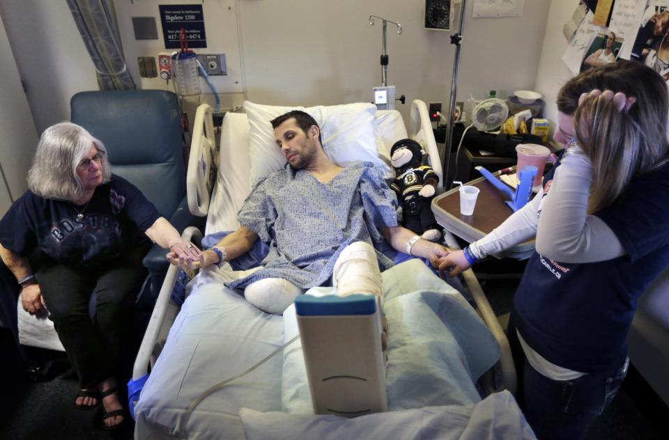 FILE - In this Thursday, May 9, 2013 file photo, Marc Fucarile, center, holds hands with his mother, Maureen Fucarile, left, and his fiancee, Jennifer Regan, right, in his room at Massachusetts General Hospital in Boston. Fucarile was only feet away from one of the Monday, April 15, 2013 bomb blasts near the finish line of the Boston Marathon that resulted in the loss of one leg, severe damage to the other, as well as burns, and a piece of shrapnel lodged in his heart. (AP Photo/Steven Senne, File)