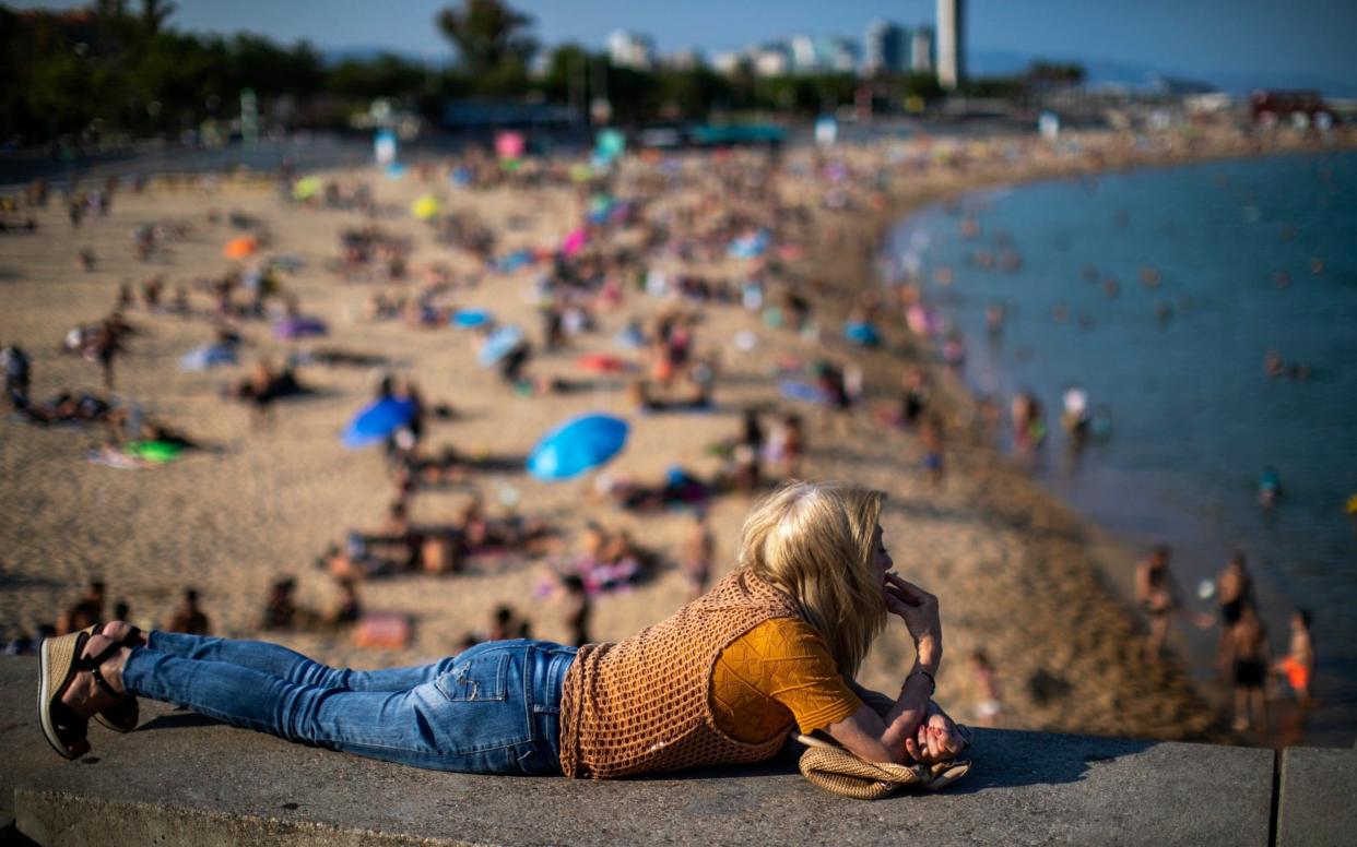 A woman smokes lying on a wall as people enjoy the beach in Barcelona - Emilio Morenatti/AP