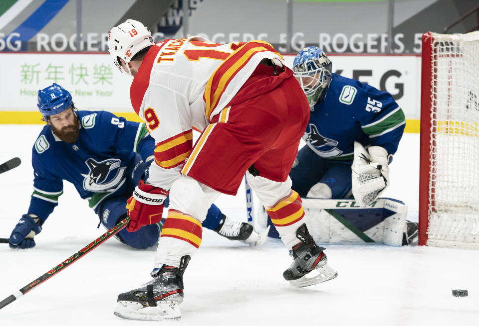 Vancouver Canucks defenseman Jordie Benn (8) tries to stop Calgary Flames left wing Matthew Tkachuk (19) from getting a shot on Canucks goaltender Thatcher Demko (35) during the first period of an NHL hockey game Thursday, Feb. 11, 2021, in Vancouver, British Columbia. (Jonathan Hayward/The Canadian Press via AP)
