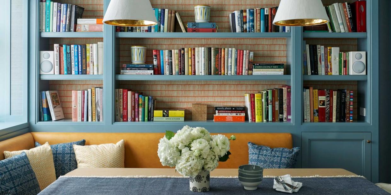 a banquette upholstered in orange surrounding a table with a vase of flowers and against a sky blue shelf