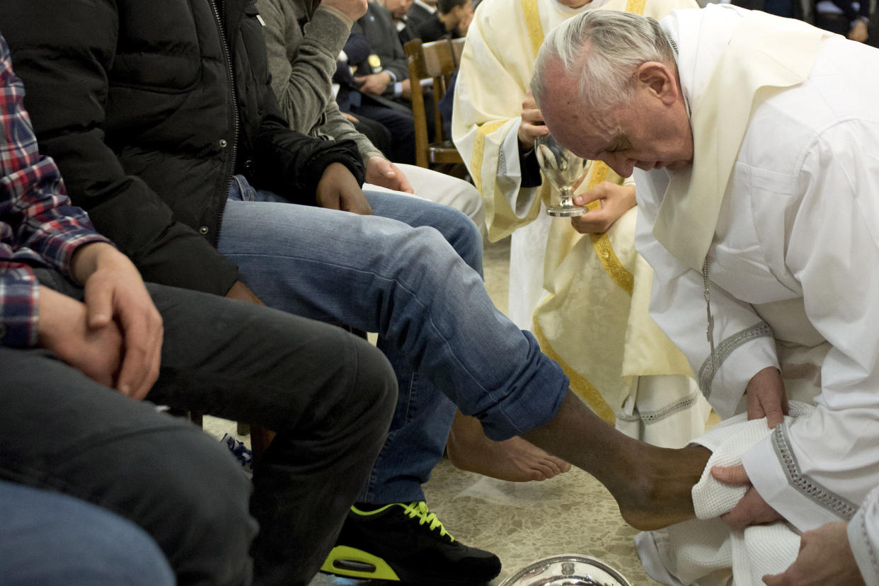 Pope Francis holds the bare foot of someone sitting among others.