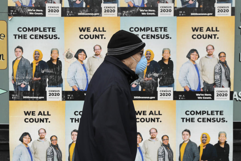 FILE - In this April 1, 2020, file photo, a man wearing a mask walks past posters encouraging participation in the 2020 Census in Seattle's Capitol Hill neighborhood. A delay in census data is scrambling plans in some states to redraw districts for the U.S. House and state legislatures. The Census Bureau has said redistricting data that was supposed to be provided to states by the end of March won't be ready until August or September. (AP Photo/Ted S. Warren, File)