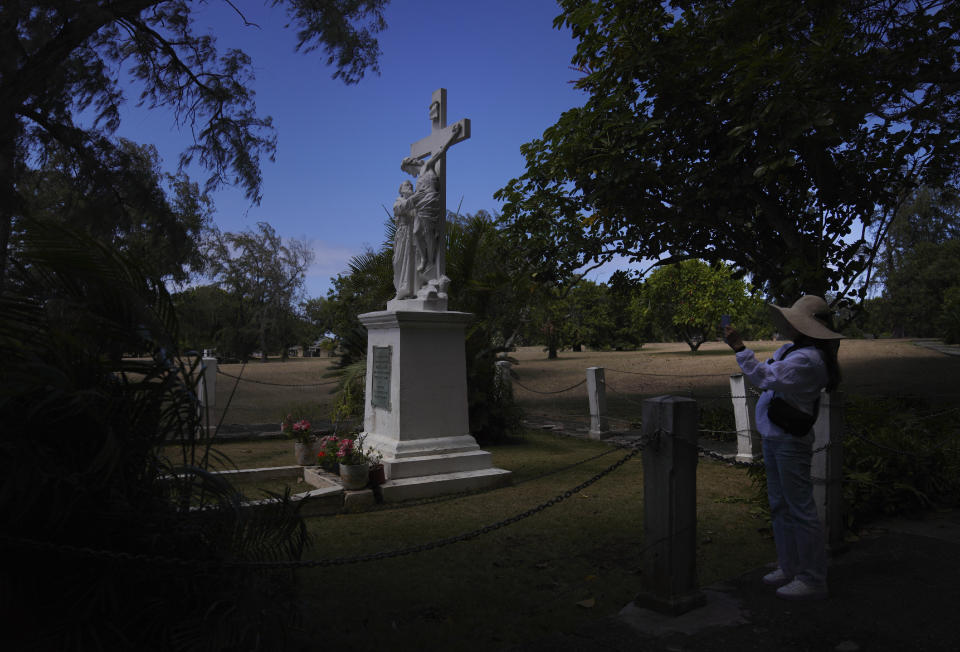 Yunra Huh, takes a photo of her family at the grave of Saint Marianne in Kalaupapa, Hawaii, on Tuesday, July 18, 2023. Huh made a pilgrimage to the remote peninsula where Catholic missionaries known as Father Damien and Mother Marianne cared for banished leprosy patients in the 1800s. (AP Photo/Jessie Wardarski)