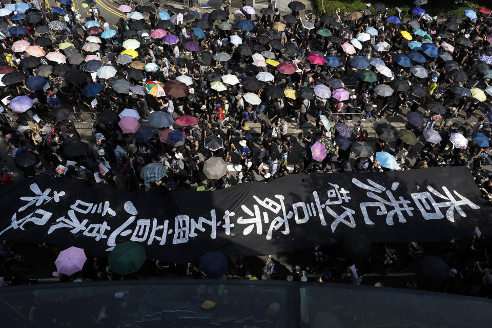 Manifestantes con paraguas y una enorme pancarta con las palabras "La policía de Hong Kong asesina de forma deliberada" marchan por la calle en Hong Kong, el domingo 20 de octubre de 2019. (Foto/Mark Schiefelbein)