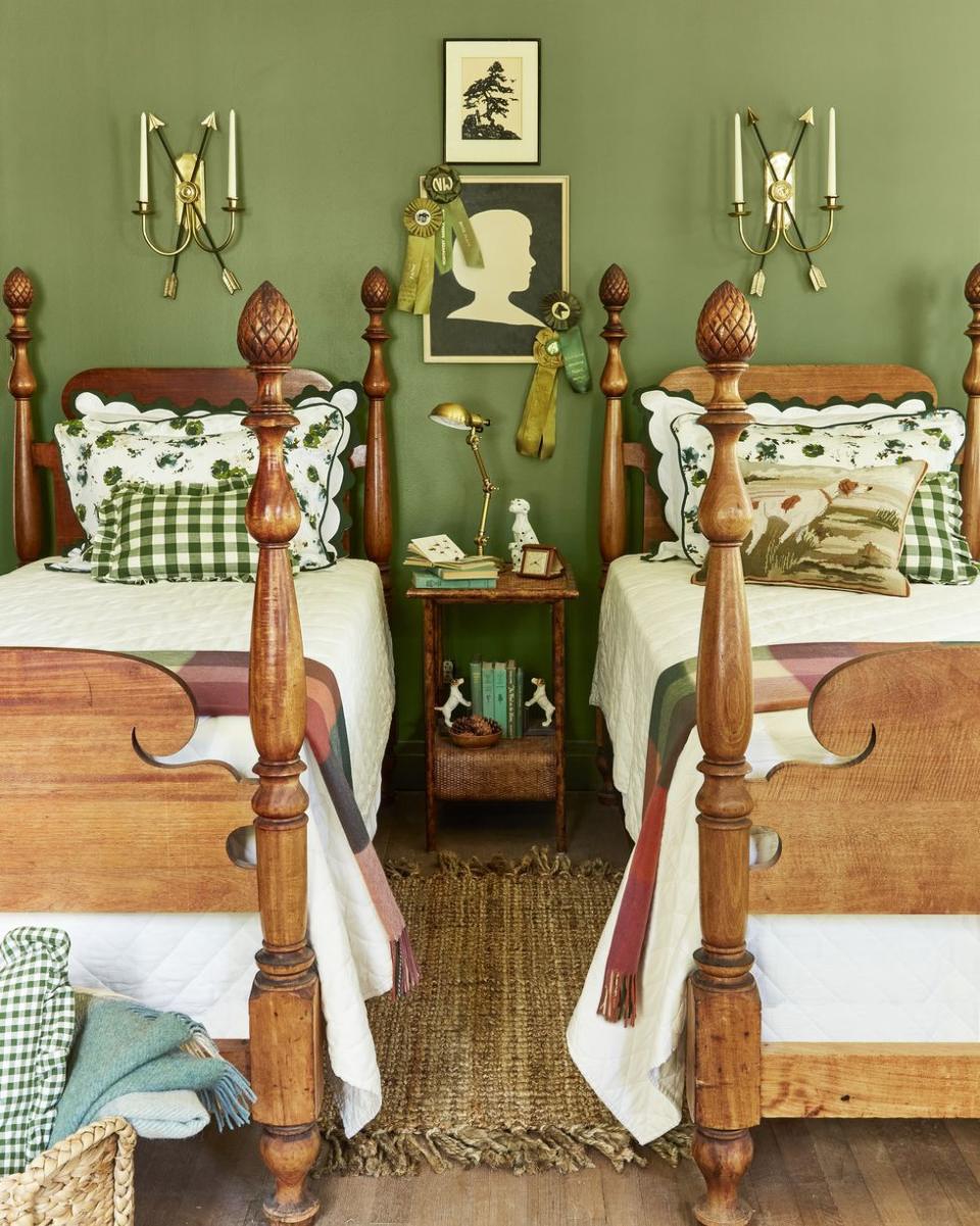 a small bedroom with earthy mossy green walls and two twin beds that are made up in green and white linens