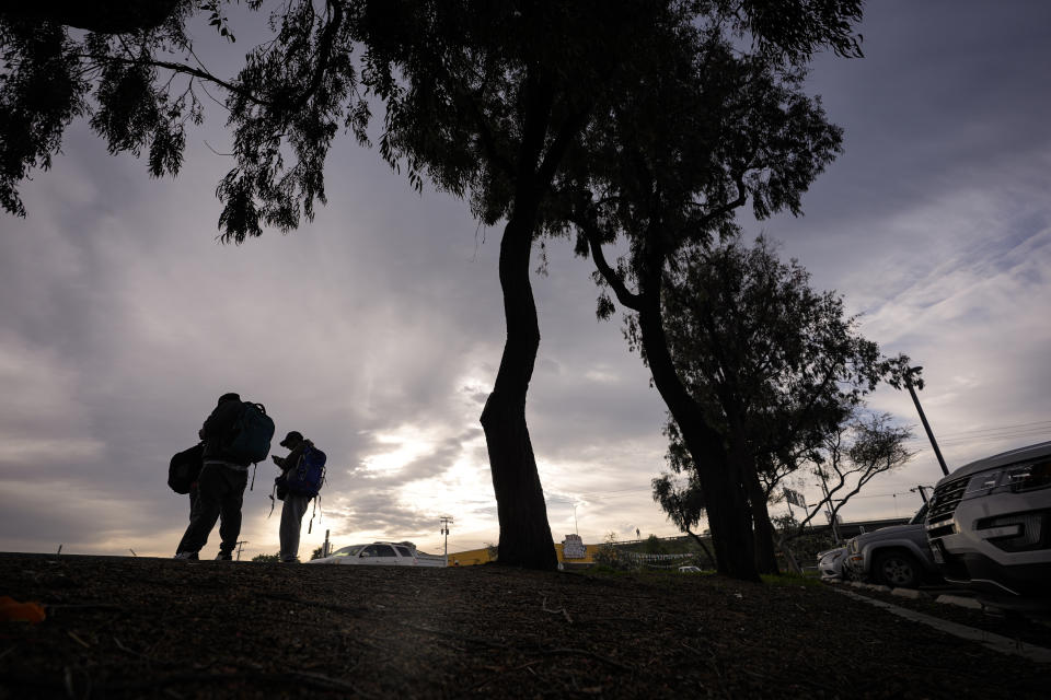 Migrants stand in groups as they arrive at a bus stop after leaving a processing facility, Friday, Feb. 23, 2024, in San Diego. Hundreds of migrants were dropped off Friday at a sidewalk bus stop amid office parks in San Diego with notices to appear in immigration court after local government funding for a reception center ran out of money sooner than expected. (AP Photo/Gregory Bull)