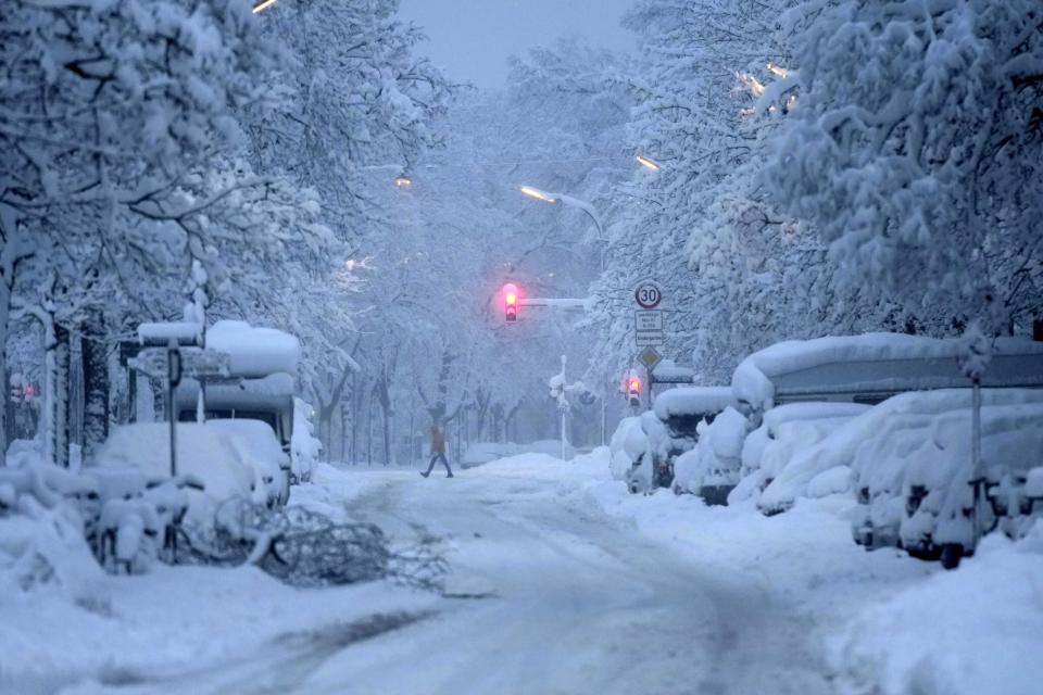 A man crosses a road early morning after heavy snow fall in Munich, Germany, Saturday, Dec. 2, 2023. (AP Photo/Matthias Schrader)